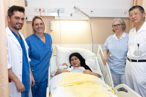 Das oberösterreichische Neujahrsbaby Minel mit seiner Mutter Aynur im Krankenbett mit vier Mitarbeiter:innen des Krankenhauses Wels-Grieskirchen
