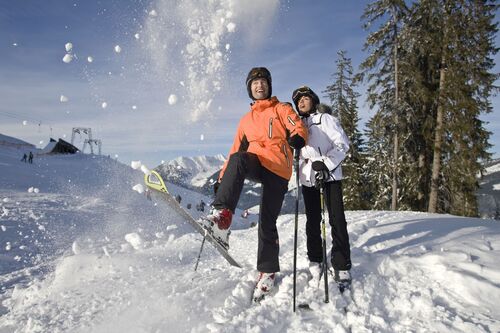 Skifahrerin und Skifahrer auf einer Schneepiste, verschneite Berge, Skilift im Hintergrund