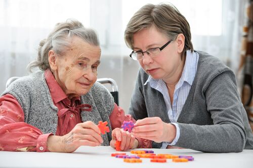Pflegekraft baut ein Puzzle mit einer betagten Dame