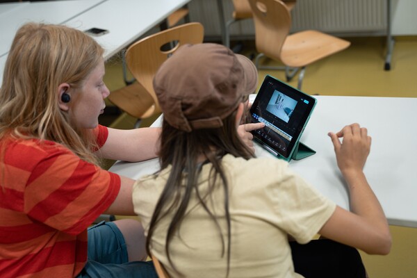 Zwei Jugendliche sitzen vor einem Tablet und schneiden gerade ein Video. 