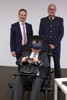 Mag. Harald Großauer und Oberst Klaus Scherleitner stehen nebeneinander, Landesrat Mag. Günther Steinkellner sitzt vor ihnen auf einem Autositz mit Lenkrad, mit Virtual Reality Brille und Kopfhörern