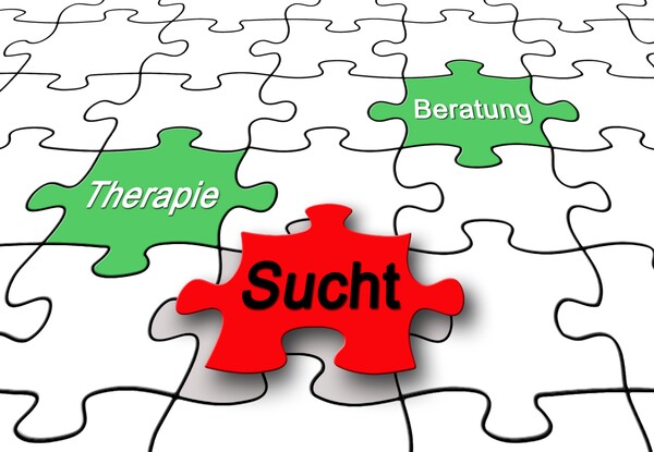 Drei mit Sucht, Therapie bzw. Beratung beschriftete Puzzleteile in einem ansonsten farblosen Puzzle