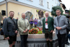 Franz Eisl, Hans Pum, Landesrat Markus Achleitner und Günter Nierlich  stehen vor der mit Blumen geschmückten Gedenkstätte aus Stein, darauf in Bronze Schneeflocken und ein Porträt von Rudi Nierlich sowie Gedenkschrift