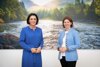 Ministerin Elisabeth Köstinger und Agrar-Landesrätin Michaela Langer-Weninger stehen vor einer Wand an der sich ein Landschaftsbild befindet (Wasser, Gebirge und Wälder)