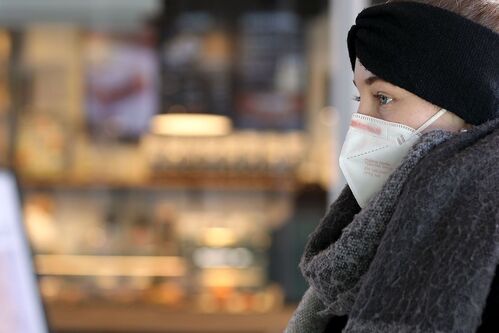 Portrait einer Jugendlichen mit FFP2-Maske, Schal und Stirnband in einem Kaufgeschäft vor einer Vitrine