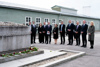 Eine Gruppe von Personen, darunter Bundeskanzler Karl Nehammer, Vizekanzler Werner Kogler, Außenminister Alexander Schallenberg, Nationalratspräsident Wolfgang Sobotka und OÖs Landeshauptmann-Stellvertreterin Christine Haberlander stehen im Freien vor einem Mahnmal für die Opfer von Kriegen, vor dem Rosen abgelegt sind. Im Hintergrund Baracken. 