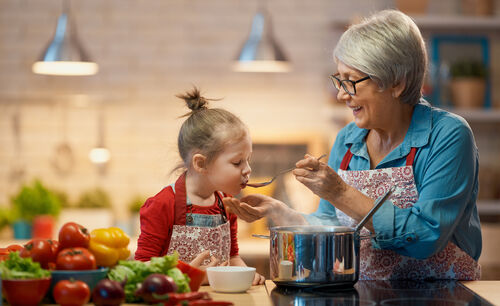 Die Oma kocht mit ihrer Enkelin im Kindergartenalter, die von ihr betreut wird, eine Gemüsesuppe und lässt sie kosten