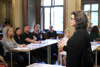 Landesrätin Birgit Gerstorfer steht in einem Repräsentationsraum im Linzer Landhaus vor Personen, die an Tischen sitzen und zuhören