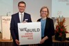 Landesrat Markus Achleitner und Ministerin Leonore Gewessler stehen nebeneinander und halten ein Schild mit Beschriftung WEBUILD Energiesparmesse Wels