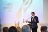 Landesrat Markus Achleitner steht vor Publikum auf einer Bühne bei einem Rednerpult mit Mikrofon, im Hintergrund Videowand mit Beschriftung WEBUILD Energiesparmesse Wels