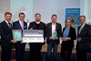 Vizebürgermeister Gerhard Kroiß, Landesrat Markus Achleitner, Lorenz Huemer und Günther Huemer, Ministerin Leonore Gewessler und Dr. Gerhard Dell stehen nebeneinander und halten Urkunde, Scheck und Preis in Händen