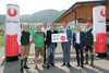 Bernhard Lankmaier, Thomas Groschl, Johannes Rumplmayr, Wolfgang Bammer, Landesrat Markus Achleitner, Franz Schiefermair und Rudi Raffelsberger stehen nebeneinander vor dem Eingangstor eine Gebäudes, Landesrat Achleitner hält ein Schild mit Aufschrift Infrastrukturoffensive, Sport Oberösterreich