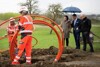 Ministerin Elisabeth Köstinger und Landesrat Markus Achleitner stehen nebeneinander unter einem Regenschirm, neben ihnen Martin Wachutka, alle begutachten eine Baustellengrube, in der zwei Arbeiter Kabel verlegen