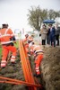 Ministerin Elisabeth Köstinger und Landesrat Markus Achleitner stehen nebeneinander unter einem Regenschirm und begutachten eine Baustellengrube, in der drei Arbeiter Kabel verlegen