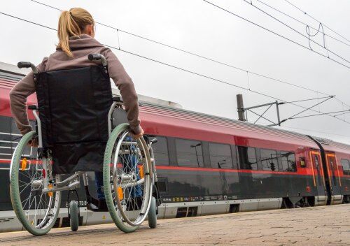 Junge Frau sitzt in einem Rollstuhl auf einem Bahnhof