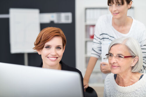 Drei Frauen unterschiedlichen Alters blicken auf einen Bildschirm und arbeiten gemeinsam an einem Projekt. 