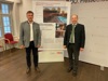 Josef Frauscher und Landesrat Max Hiegelsberger vor einem Plakat mit dem Bild eines Badehauses aus Holz, Terrasse und Schwimmbad