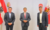 Markus Friesacher, Landesrat Markus Achleitner und Mag. Stefan Krapf stehen nebeneinander, im Hintergrund Österreich- und Oberösterreich-Fahne