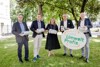 Dr. Thomas Poltura (Alpenverein Oberösterreich), Umwelt- und Klima-Landesrat Stefan Kaineder, Silvia Huber, MPA (FAB), Bgm. Roland Wohlmuth und DI Thomas Anderer (beide LAV OÖ) stehen nebeneinander im Landhauspark, sie halten alle einen Upcycling-Hüttenschlafsack in Händen, Wohlmuth und Anderer halten zusätzlich ein Schild mit der Aufschrift „Unsere Umweltprofis“.