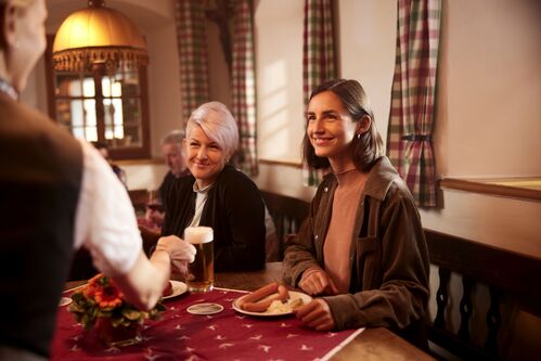 Kellner serviert zwei Frauen in einer Gaststube ein Bier