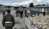 Gruppenbild mit Bundesministerin Mag. Klaudia Tanner und Landesrat Markus Achleitner, die Personengruppe steht vor einem Sarkophag im Hof der Gedenkstätte Mauthausen, seitlich Barackengebäude