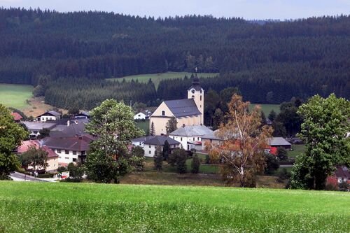 Dorf mit Kirche in einer Landschaft mit Wiesen und Wäldern