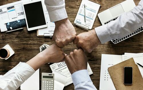 Vier Hände über einem Schreibtisch deuten Zusammenarbeit an