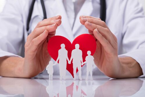 Hände einer Ärztin breiten sich schützend über das Symbol einer Familie, dahinter ein Herz