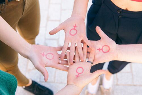 Vier Frauenhände berühren einander, auf jeder Handinnenfläche ist das Symbol für Weiblichkeit aufgemalt