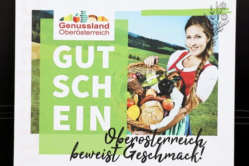 Muster für einen Gutschein mit der Aufschrift: „Oberösterreich beweist Geschmack!“ mit einer jungen Frau im Hintergrund, die einen Korb voll regionaler Lebensmitteln hält