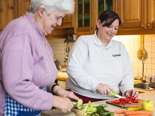 Hauskrankenpflegerin schneidet mit einer Seniorin Gemüse in der Küche