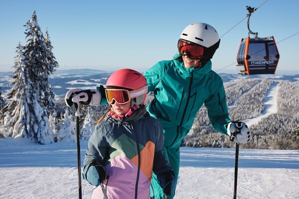 Frau und Mädchen in Schibekleidung in der Winterlandschaft des Hochfichts vor einer Gondel 
