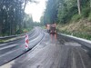 Straßenbaustelle, eine Hälfte der Straße ist fertig asphaltiert, die andere Hälfte im Bau, Baufahrzeug, Trennung der Straßenhälften durch regelmäßig aufgestellte Markierungszeichen