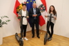 Landtagspräsident Wolfgang Stanek überreichte in einem Raum des Landhauses Corinna Denk und Dominik Felberbauer die E-Scooter, dahinter drei Fahnen – Oberösterreich, EU und Österreich. daneben ein grüner Standblumenstock.