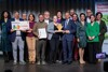 Gruppenbild mit 15 Personen stehend in zwei Reihen mit Preis, symbolischem Geldpreis und Urkunde, unter ihnen mittig und vorne Landesrat Dr. Wolfgang Hattmannsdorfer