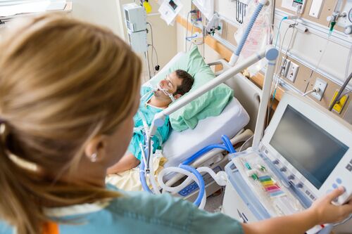 Krankenschwester drückt Monitorknöpfe, Patient liegt in Spitalsbett 