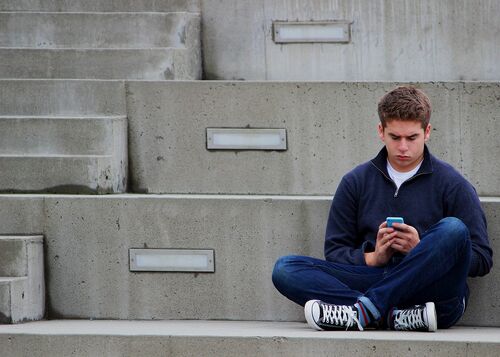 Jugendlicher, sitzend auf einer Stufe mit Smartphone beschäftigt