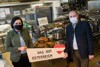 Ministerin Elisabeth Köstinger und Landesrat Max Hiegelsberger in einer Großküche, beide mit Mund-Nasen-Schutz, halten ein Holzschild mit Aufschrift „Das isst Österreich“, dahinter eine Platte mit gebratenen Gänsen