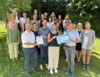 Eine Gruppe von 27 Personen steht in mehreren Reihen in einem Garten, in der ersten Reihe Günther See, Mag. Norbert Rainer, Martina Weikl und Landesrat Stefan Kaineder nebeneinander mit Urkunde und Tafel in Händen