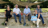 Mag.a Heidi Stacherl, Günther See, Landesrat Stefan Kaineder, Martina Weikl mit Tafel in Händen und Mag. Norbert Rainer sitzen nebeneinander auf der Umrandung eines Sandspielplatzes