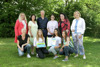 Eine Gruppe von zehn Personen in zwei Reihen auf einer Wiese, im Hintergrund Bäume und Sträucher