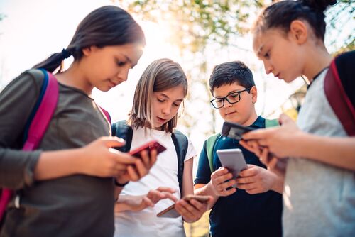 Vier Kinder mit Smartphones in Händen stehen nebeneinander im Halbkreis