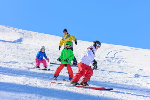 Drei Kinder und ein Erwachsener skifahrend auf einer schneebedeckten Piste