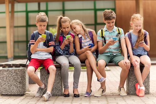 Fünf Kinder sitzen auf einer Bank, alle schauen auf ein Handy