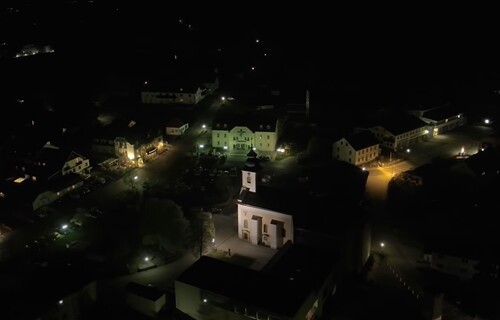 Blick aus der Vogelperspektive auf ein Dorf mit Kirche, Straßenbeleuchtung