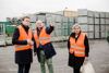 Landesrat Stefan Kaineder, DI Christian Ehrengruber und Bürgermeisterin Daniela Durstberger stehen nebeneinander auf einem Lagerplatz, im Hintergrund große gestapelte Behälter