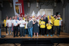 Gruppenbild mit 27 Personen in drei Reihen auf einer Bühne, Landeshauptmann Mag. Thomas Stelzer und Landesrat Markus Achleitner inmitten der Special Olympics-Teilnehmerinnen und -Teilnehmern