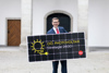 Landesrat Markus Achleitner mit einem Photovoltaik-Paneel mit Aufschrift OÖ Photovoltaik Strategie 2030 und stilisiertes Kabel in Form einer Sonne
