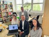 Landesrat Dr. Wolfgang Hattmannsdorfer sitzt gemeinsam mit Projektleiterin Nicole Sevik, Obmann Sefa Yetkin und Geschäftsführerin Fatima Malic in einem Büro; vor ihnen steht ein aufgeklappter Laptop am Tisch, im Hintergrund ist ein Regal mit vielen Büchern zu sehen.