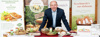 Landesrat Max Hiegelsberger stützt sich auf einen Ausstellungstisch, auf dem verschiedene Lebensmitteln präsentiert sind, im Hintergrund Rollplakate der Betriebe Gustino, Sauwald Erdäpfel, Nudelmanufaktur Huber und Genussland Oberösterreich